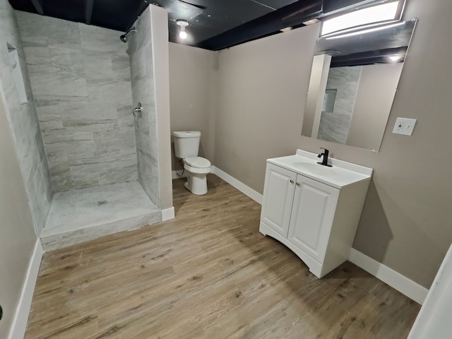 bathroom with toilet, wood finished floors, tiled shower, baseboards, and vanity