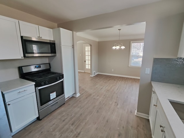 kitchen with light wood-type flooring, stainless steel appliances, arched walkways, white cabinets, and a chandelier