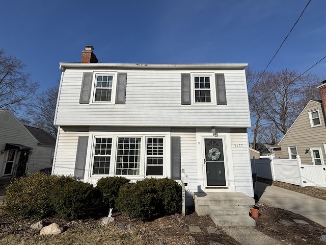 colonial-style house featuring a chimney and fence