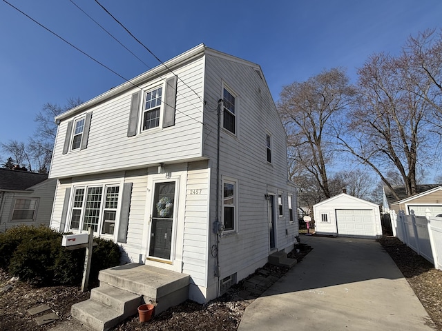 colonial inspired home with an outbuilding, concrete driveway, a detached garage, and fence