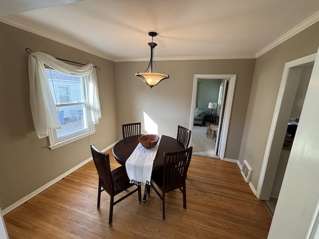 dining area featuring visible vents, baseboards, wood finished floors, and crown molding