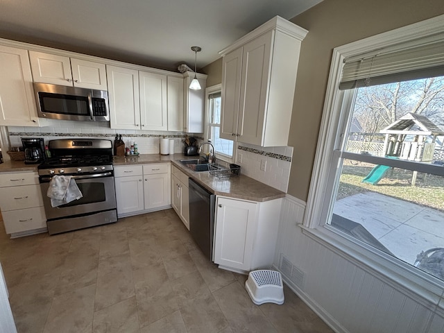 kitchen featuring a wainscoted wall, a sink, tasteful backsplash, appliances with stainless steel finishes, and white cabinets