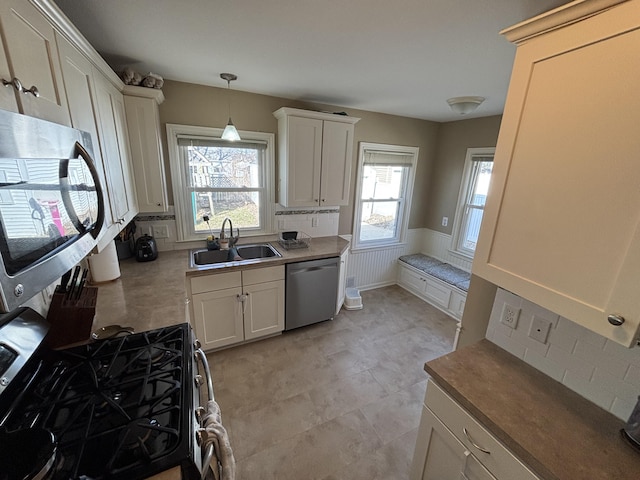 kitchen featuring pendant lighting, wainscoting, white cabinets, stainless steel appliances, and a sink