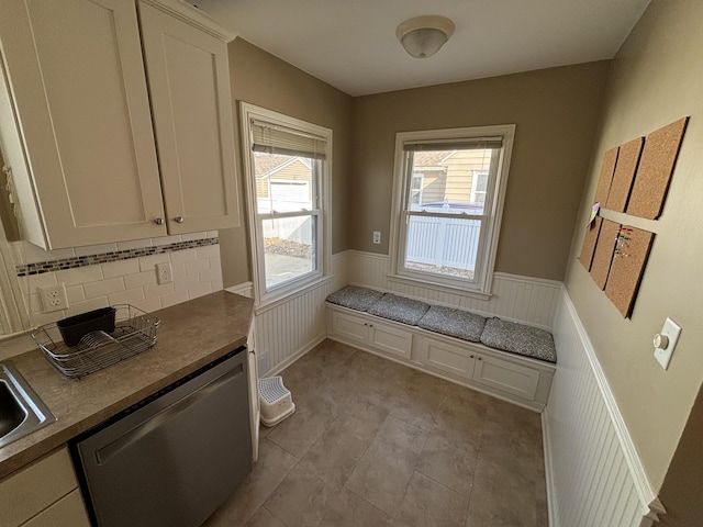 kitchen with a sink, tasteful backsplash, white cabinets, wainscoting, and dishwasher