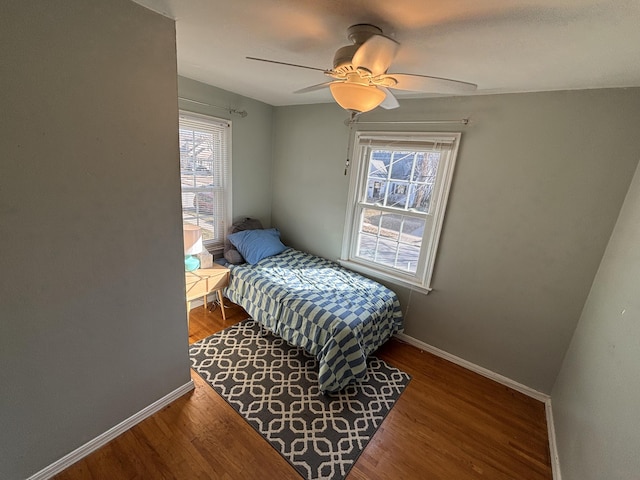 bedroom with multiple windows, a ceiling fan, baseboards, and wood finished floors