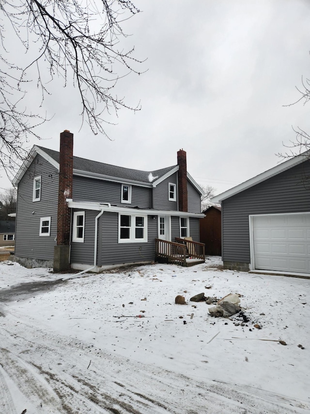 snow covered property with a deck, a chimney, a garage, and an outdoor structure