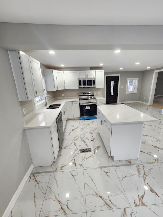 kitchen featuring a kitchen island, baseboards, recessed lighting, appliances with stainless steel finishes, and a sink