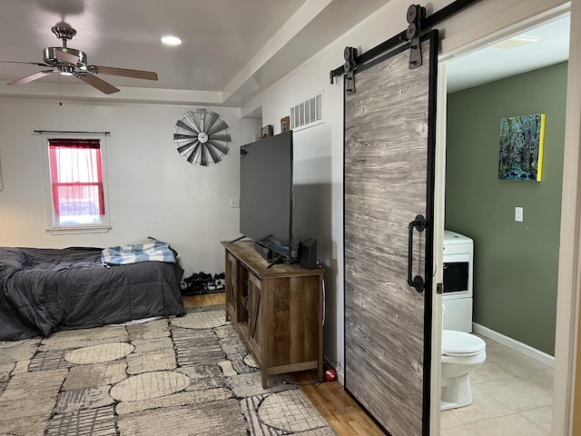 bedroom with wood finished floors, visible vents, baseboards, a barn door, and a raised ceiling