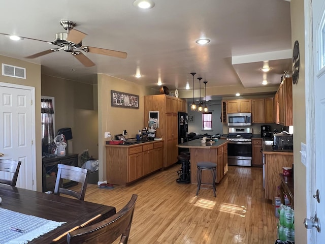 kitchen featuring a center island, ceiling fan, a breakfast bar area, brown cabinets, and stainless steel appliances