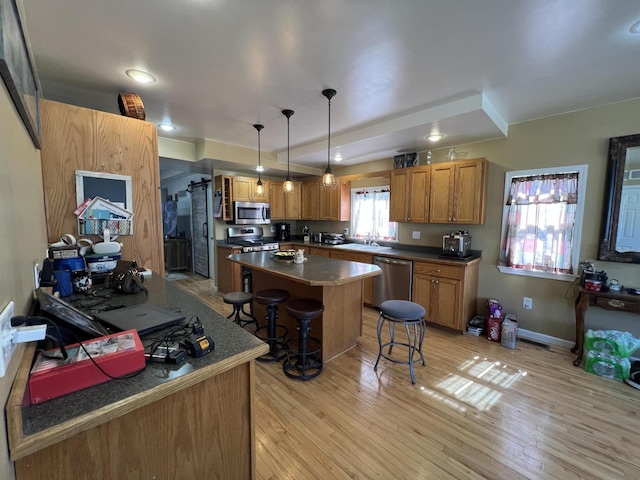 kitchen featuring brown cabinets, a kitchen breakfast bar, a center island, light wood-style floors, and appliances with stainless steel finishes