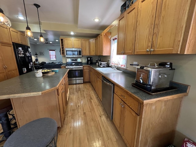 kitchen featuring dark countertops, light wood finished floors, a center island, appliances with stainless steel finishes, and a sink