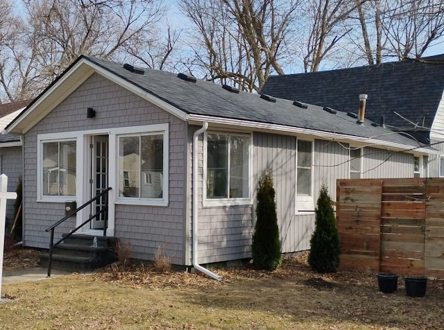 view of front of property with entry steps, roof with shingles, and fence