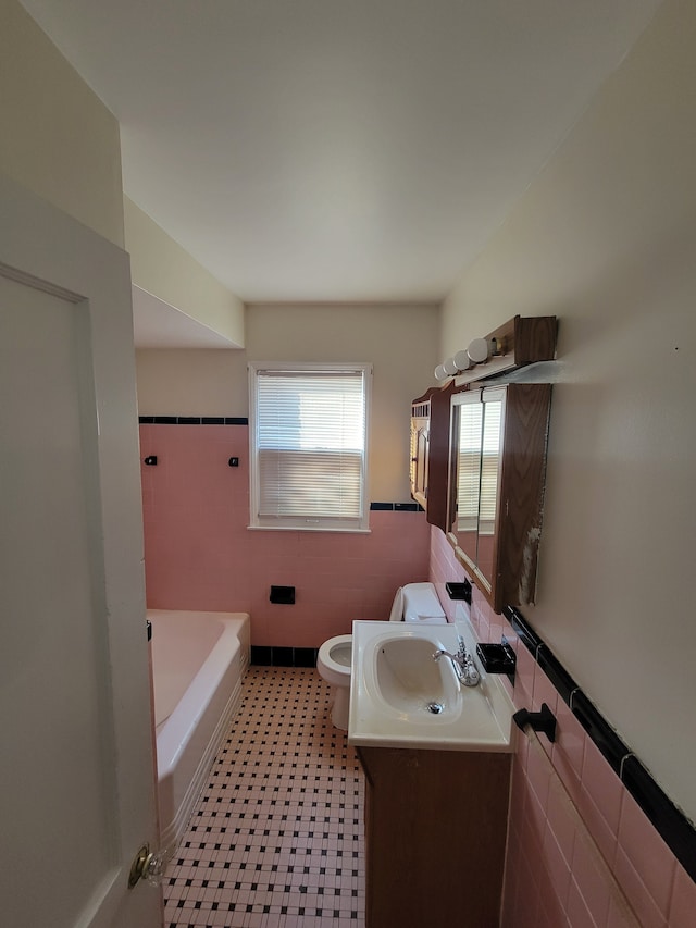 bathroom featuring a wainscoted wall, toilet, a bathing tub, tile walls, and vanity