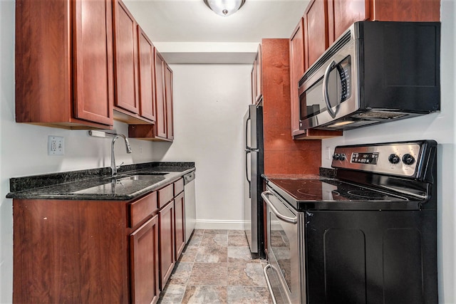 kitchen with stone finish flooring, a sink, dark stone counters, baseboards, and appliances with stainless steel finishes