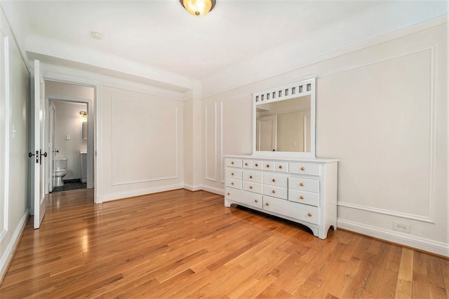unfurnished bedroom with baseboards, a decorative wall, and light wood-style flooring