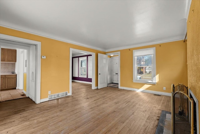 unfurnished living room featuring light wood-type flooring, visible vents, baseboards, and ornamental molding