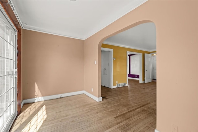 empty room with visible vents, baseboards, ornamental molding, hardwood / wood-style floors, and arched walkways