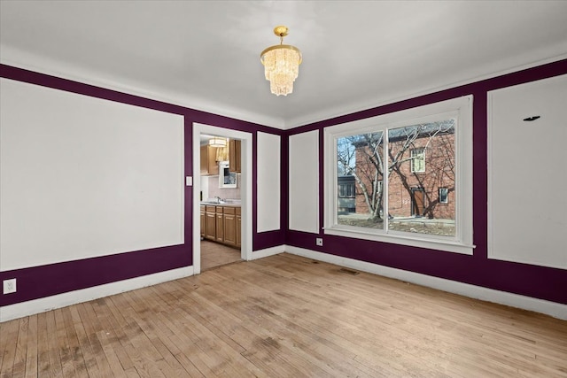 unfurnished room with visible vents, baseboards, light wood-type flooring, and an inviting chandelier