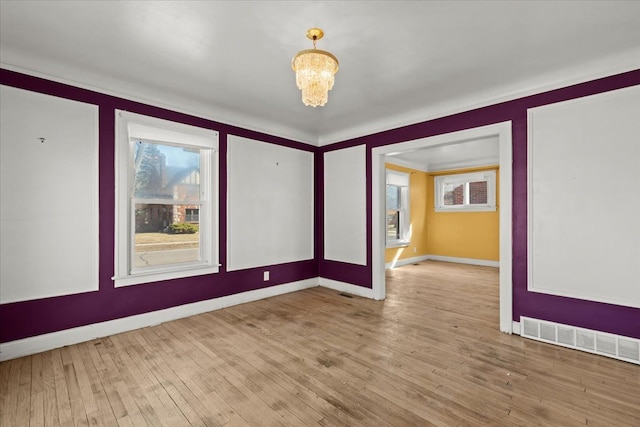 spare room featuring a wealth of natural light, a notable chandelier, visible vents, and wood finished floors