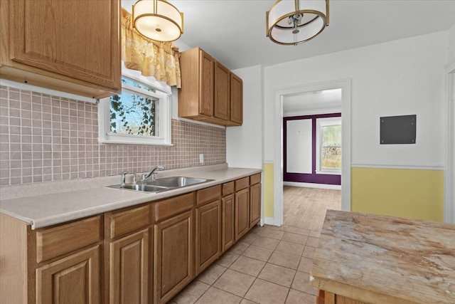 kitchen with a sink, tasteful backsplash, light countertops, light tile patterned floors, and baseboards