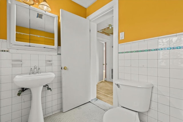 bathroom with a sink, tile walls, toilet, and wainscoting