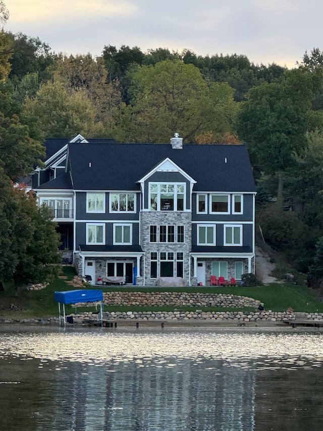 rear view of house with stone siding, a water view, and a wooded view