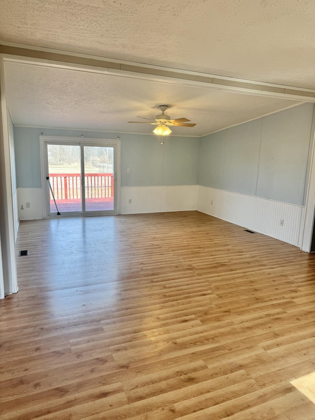 unfurnished room featuring visible vents, light wood finished floors, wainscoting, ceiling fan, and a textured ceiling