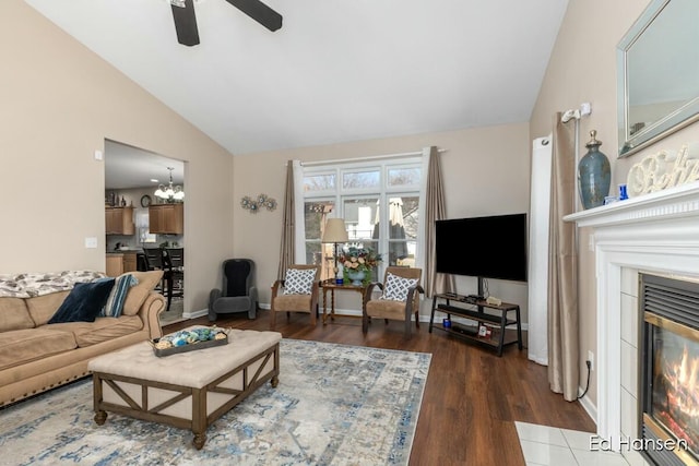 living room featuring a fireplace with flush hearth, ceiling fan with notable chandelier, wood finished floors, baseboards, and vaulted ceiling