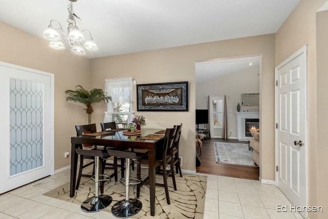 dining space featuring tile patterned flooring, a notable chandelier, baseboards, and a glass covered fireplace