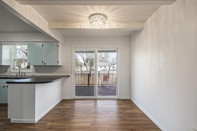 kitchen with baseboards, dark wood finished floors, beam ceiling, a sink, and dark countertops