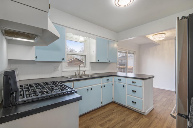 kitchen featuring blue cabinets, a sink, under cabinet range hood, plenty of natural light, and dark countertops