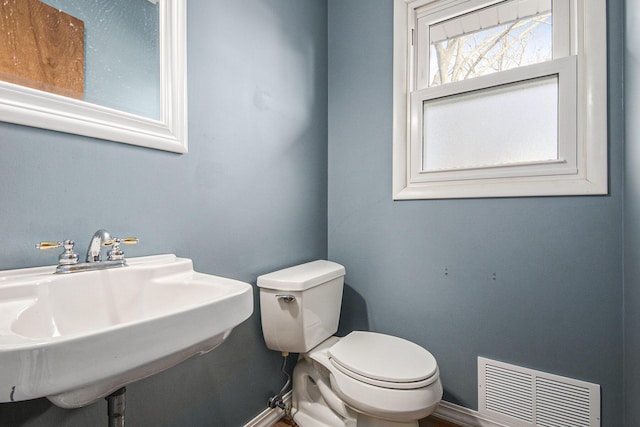 half bathroom featuring toilet, baseboards, visible vents, and a sink