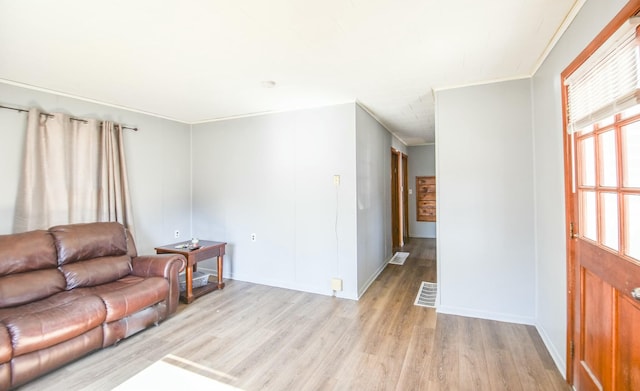 living area with crown molding, visible vents, and light wood-type flooring