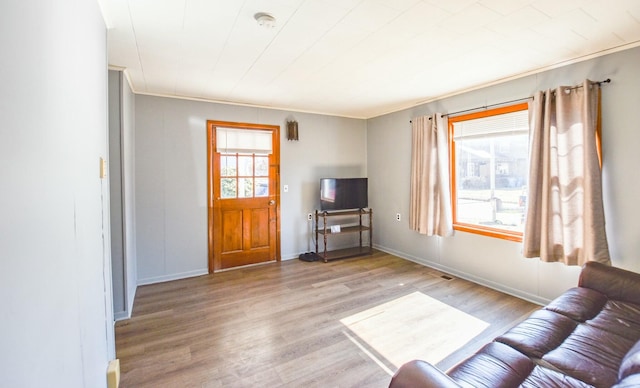 living room with light wood-type flooring, baseboards, and crown molding