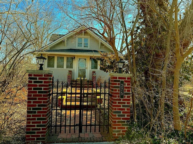 bungalow-style home with a fenced front yard, brick siding, a shingled roof, and a gate