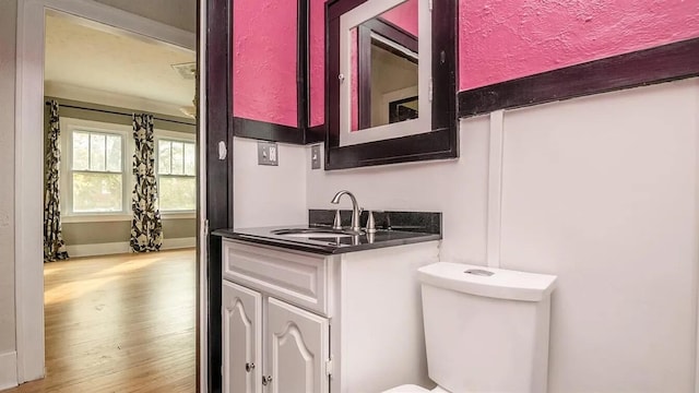 kitchen with dark countertops, baseboards, wood finished floors, white cabinets, and a sink