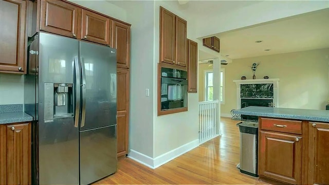 kitchen featuring oven, baseboards, fridge with ice dispenser, light wood-style flooring, and brown cabinetry