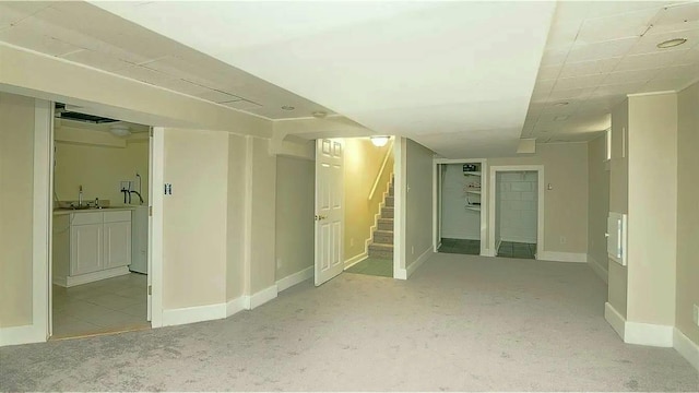 finished basement with light colored carpet, stairs, baseboards, and a sink