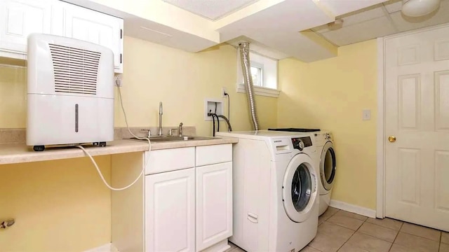 washroom featuring a sink, washing machine and dryer, cabinet space, light tile patterned floors, and baseboards