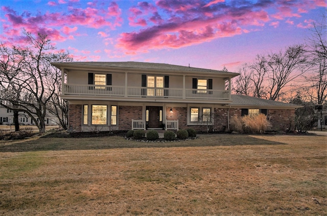 view of front of property featuring a front lawn, a balcony, brick siding, and covered porch