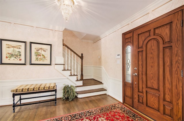 foyer entrance with crown molding, stairway, an inviting chandelier, wood finished floors, and a decorative wall