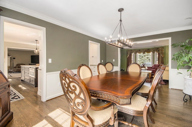 dining space featuring ornamental molding, wood finished floors, a chandelier, and wainscoting