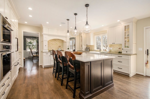 kitchen featuring a kitchen bar, glass insert cabinets, white cabinets, and light countertops