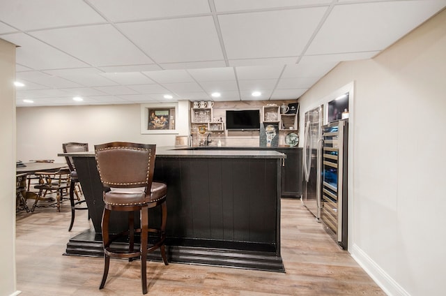 bar featuring beverage cooler, a drop ceiling, baseboards, light wood finished floors, and wet bar