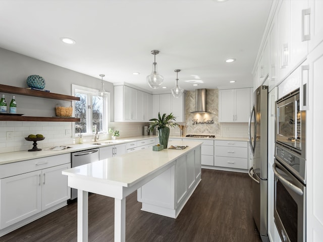 kitchen with light countertops, white cabinets, stainless steel appliances, wall chimney exhaust hood, and a sink