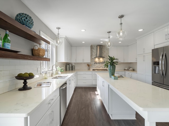 kitchen with a sink, a kitchen island, white cabinetry, stainless steel appliances, and wall chimney range hood