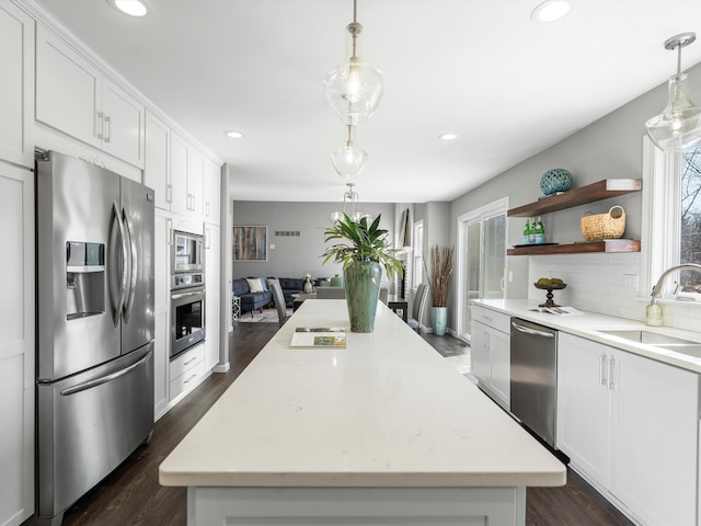 kitchen with a kitchen island, decorative backsplash, white cabinets, stainless steel appliances, and a sink