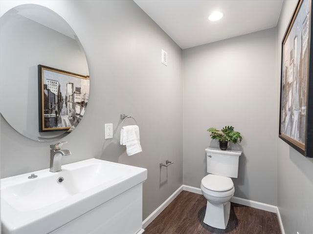 half bath with visible vents, toilet, a sink, wood finished floors, and baseboards