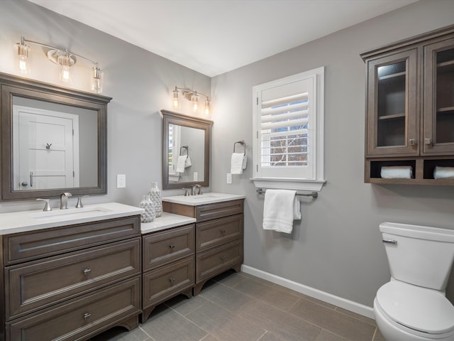 bathroom with a sink, baseboards, toilet, and double vanity