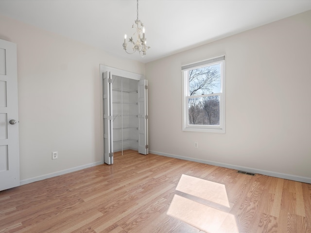 unfurnished bedroom with a chandelier, visible vents, light wood-style flooring, and baseboards